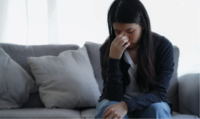 Female with ADHD fatigue looking dismayed sitting on a couch with head down