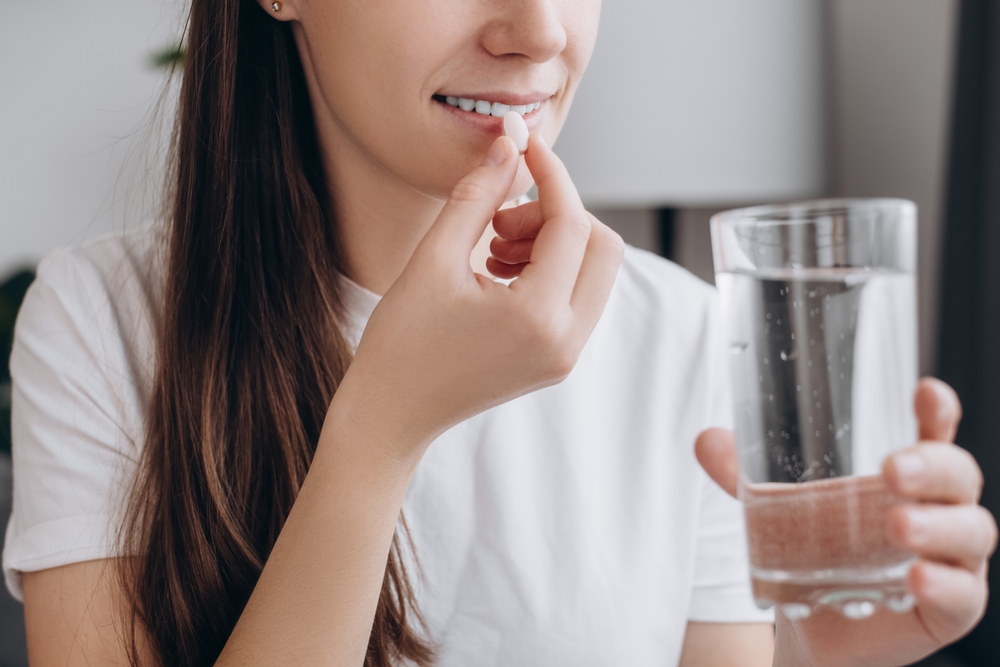 Woman taking medication tablet with glass of water