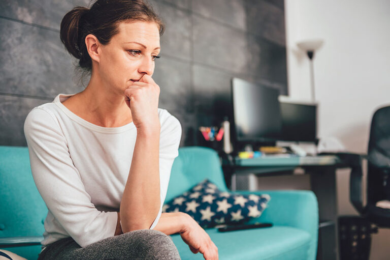 Woman sitting on couch thinking, starring down