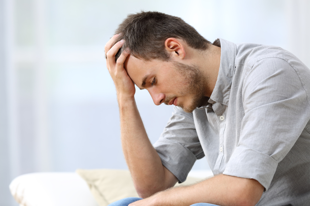 Sad man sitting with hand on forehead, looking down