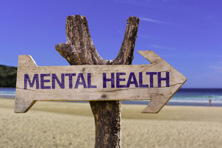 Wooden arrow sign on beach that says mental health to symbolize a healing journey.