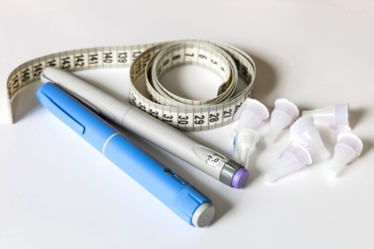 2 GLP-1 pens and a cloth tape measure to represent GLP-1 agonist medications